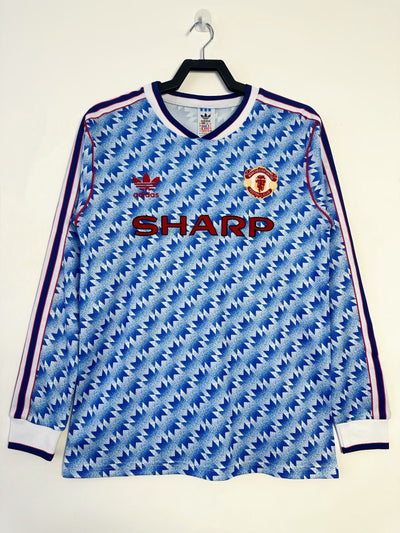 Retro Manchester United 1990-1992 away jersey by Adidas with Sharp logo, iconic blue and white geometric pattern.